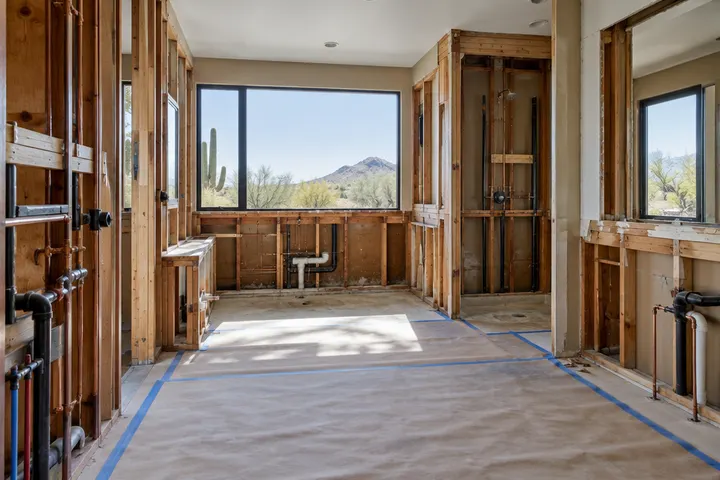 Large primary bathroom taken down to the studs during a remodel, old tub removed, plumbing exposed, floors protected